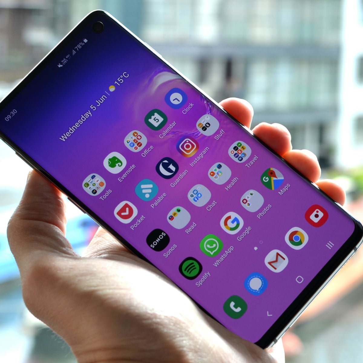 Person is holding a Samsung S10 phone in the left hand. On the background is modern building